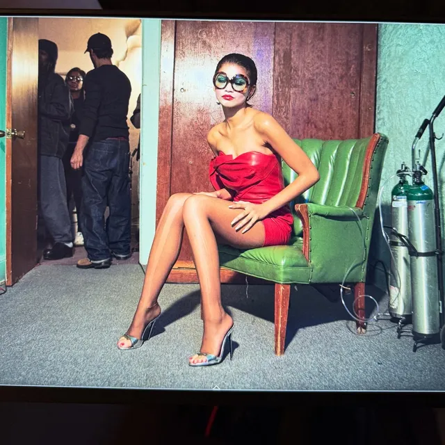 Zendaya sitting on a green chair in a red outfit.