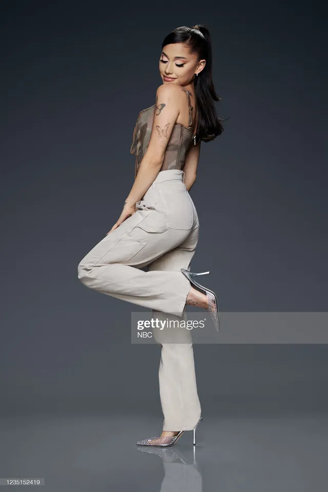 Ariana Grande posing in pale trousers and silver pointed heels.