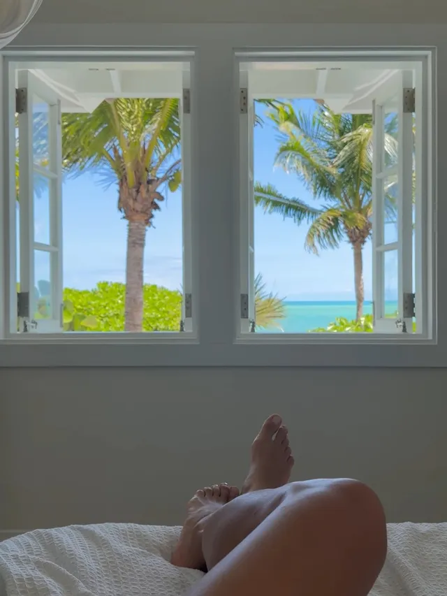 Irina Shayk relaxing beside a window overlooking palm trees.