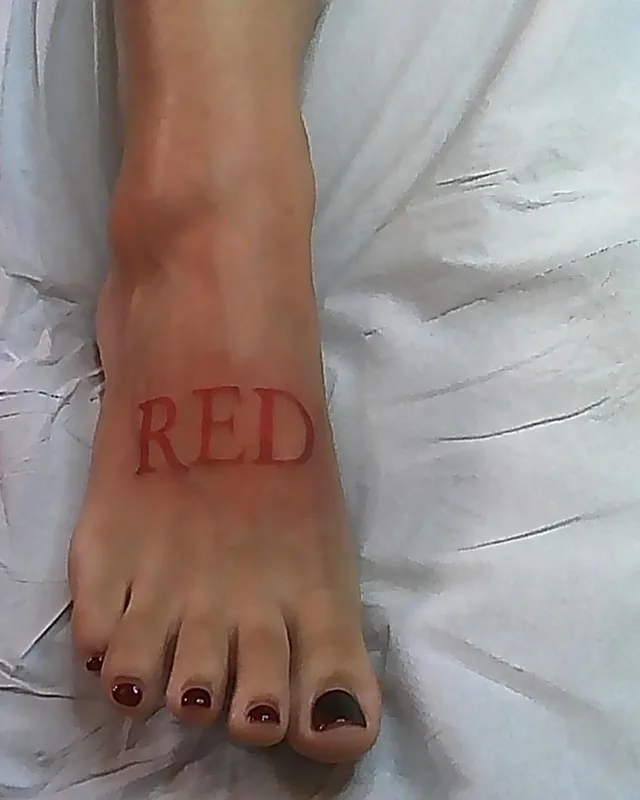 Doja Cat showing a bare foot with dark nail polish and red lettering.