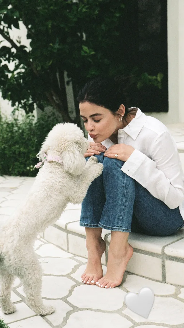 Lucy Hale greeting a white dog while seated outdoors.