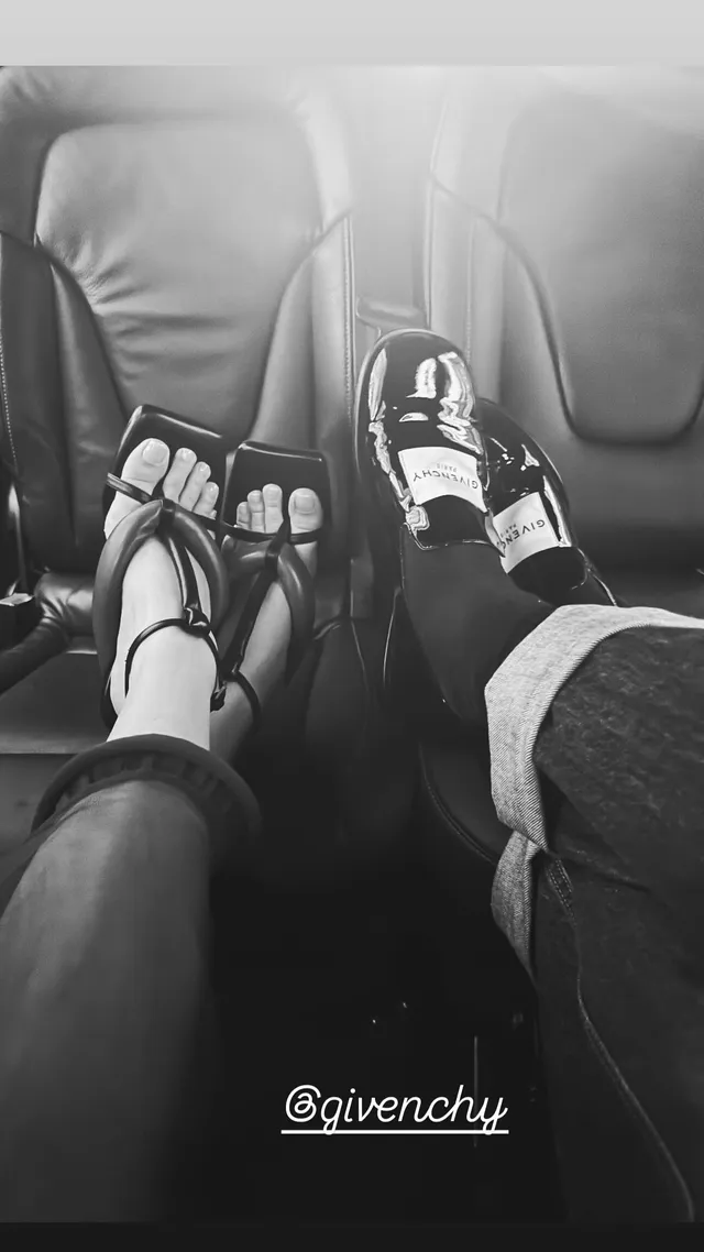 Jenna Ortega with a strappy heel visible beside another person's sneaker in a black-and-white photograph.