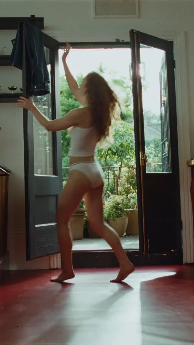 Sadie Sink walking barefoot beside open glass doors.