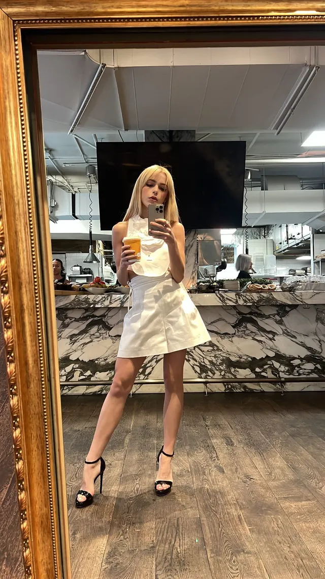 Kiernan Shipka taking a mirror selfie in a pale dress and black heels.
