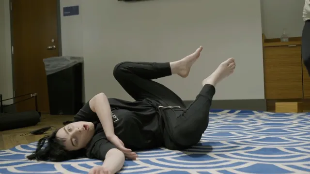 Billie Eilish a reclining black outfit on a patterned bed.