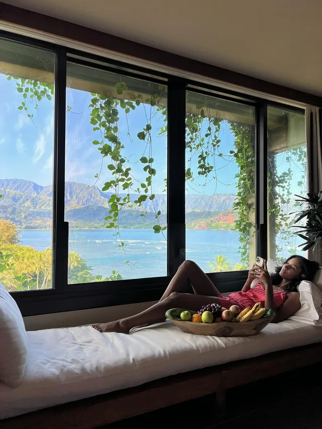 Greta Onieogou reclining barefoot beside a window with a sea view.