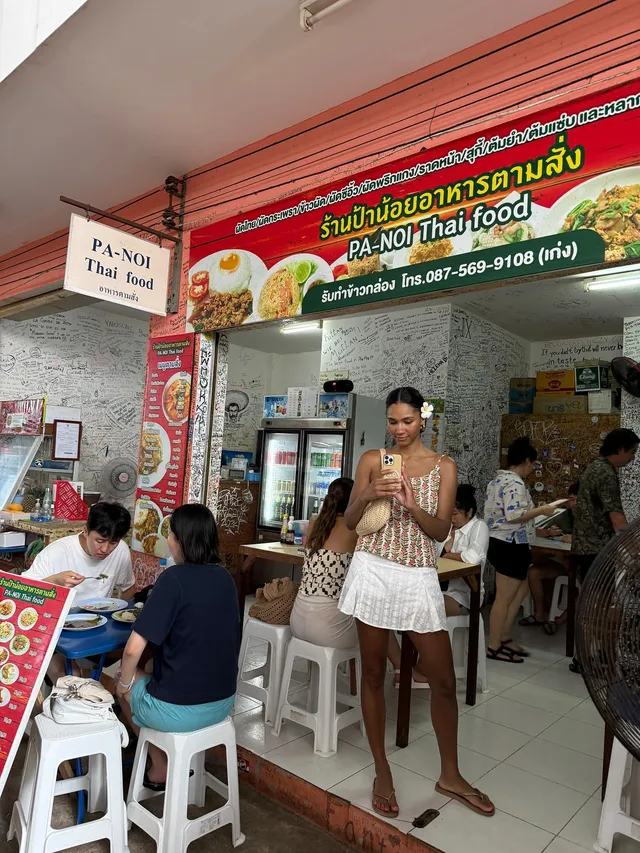 Greta Onieogou standing outside a food stall in a patterned top, white skirt and flat sandals.