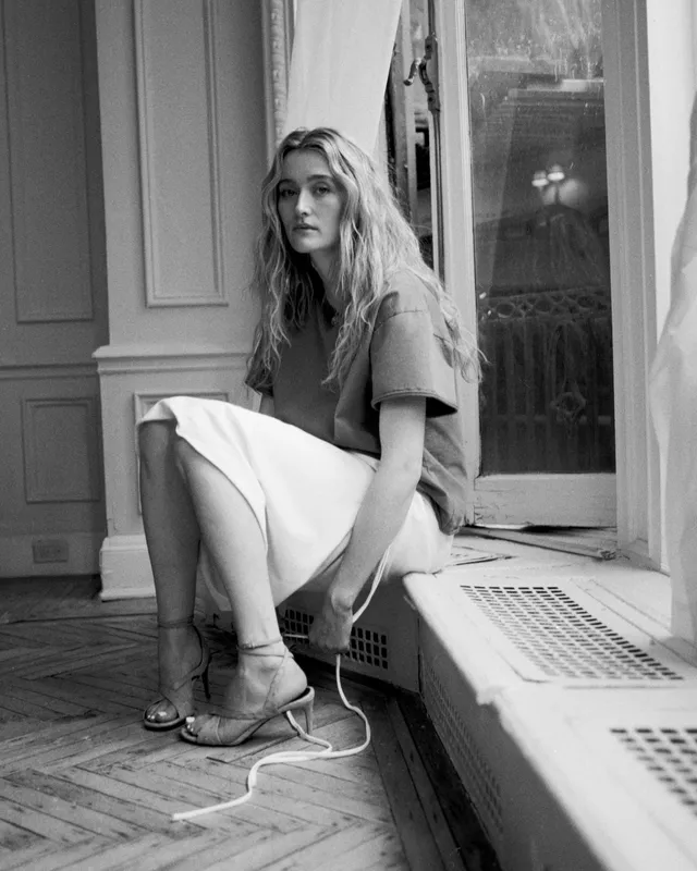 Sarah Pidgeon sitting by a window in a skirt and lace-up shoes.