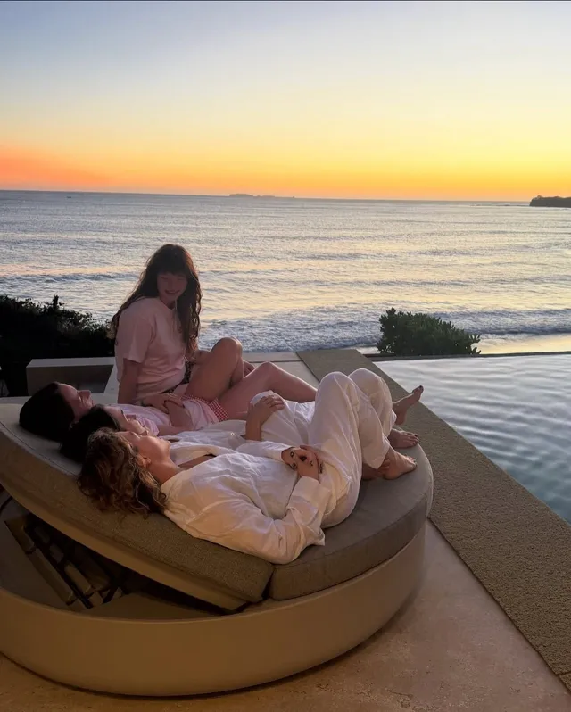 Chloë Grace Moretz relaxing barefoot with another person on a sea-view lounger.