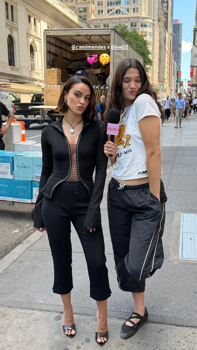 Camila Mendes posing with a friend outdoors in a black outfit and heels.