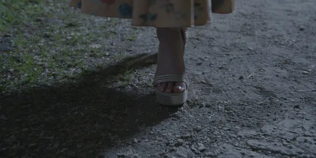 Anna Kendrick walking along a path wearing pale heeled shoes.