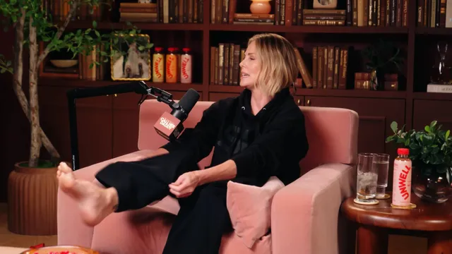 Charlize Theron seated on a talk show chair with feet raised.