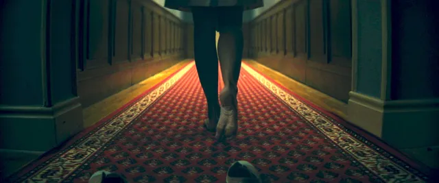 Ester Expósito walking barefoot along a patterned hallway during a screen scene.