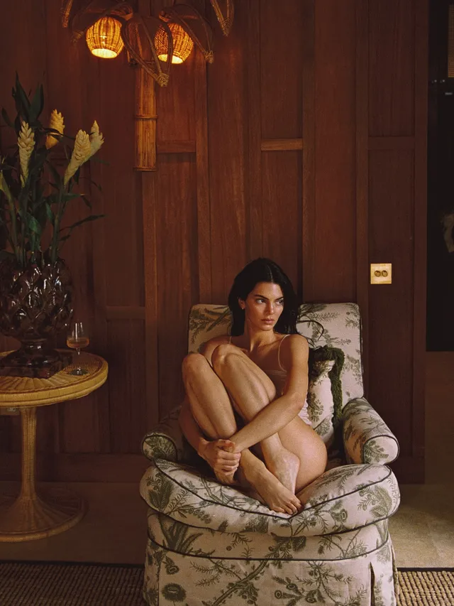 Kendall Jenner sitting barefoot in a patterned armchair.