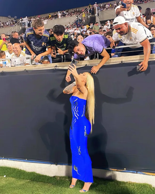 Iggy Azalea standing near spectators in a blue outfit and clear heels.