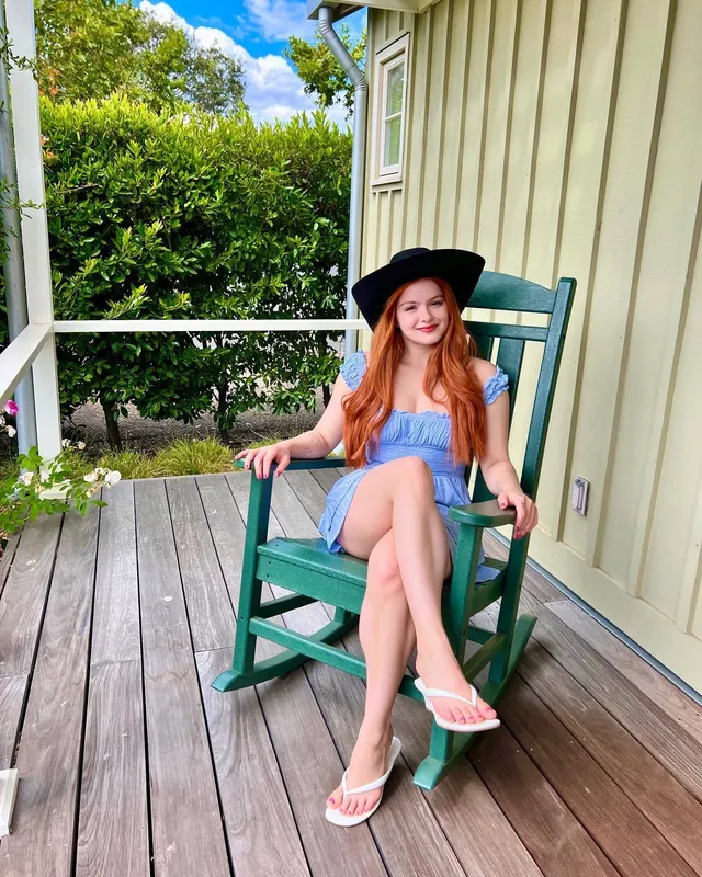 Ariel Winter sitting in a porch chair in a blue dress and flip-flops.