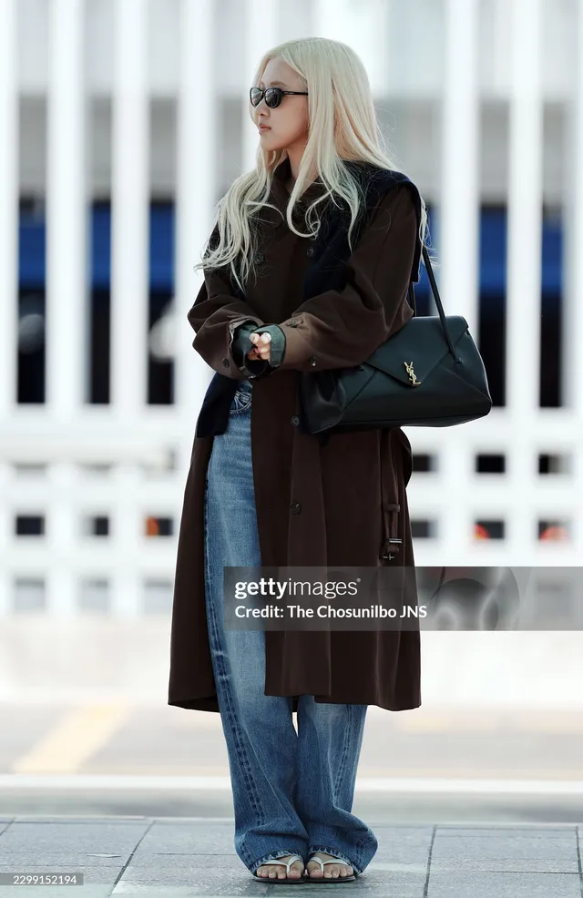 Rosé standing outside in sunglasses, a brown coat and wide-leg jeans with sandals.