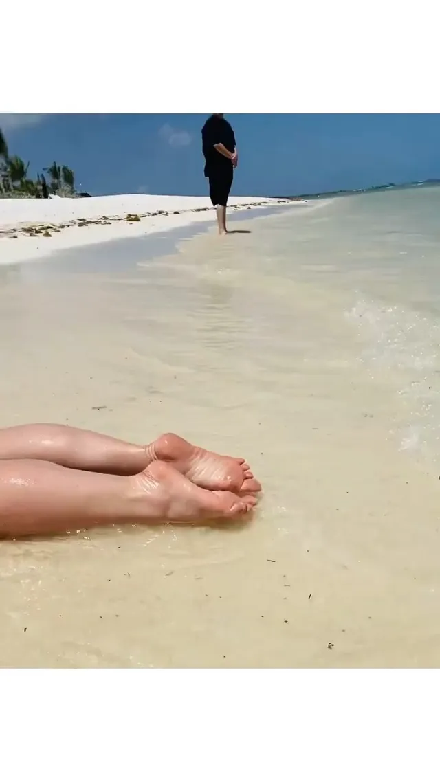Britney Spears bare feet beside shallow water on a beach.