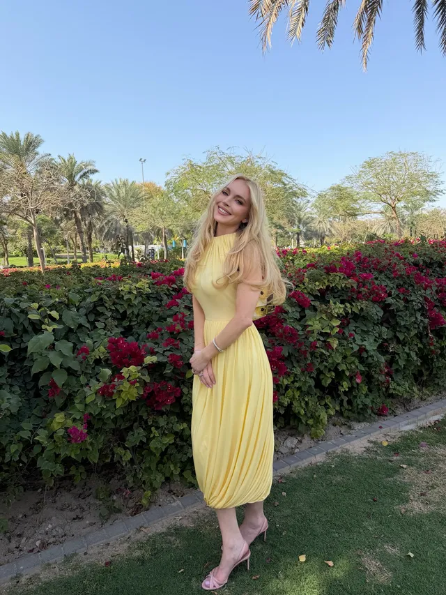 Lindsay Lohan standing outdoors in a yellow dress and sandals.