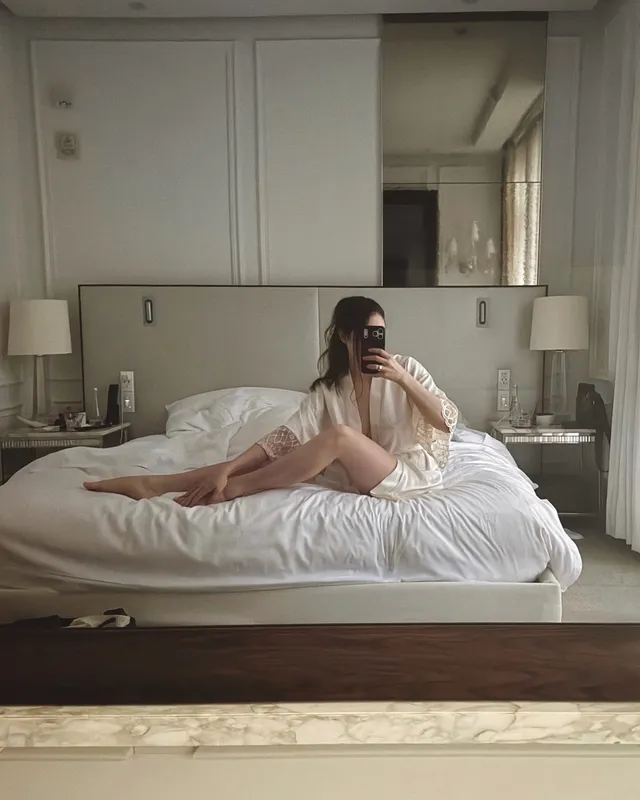 Elizabeth Gillies sitting on a bed for a mirror portrait.