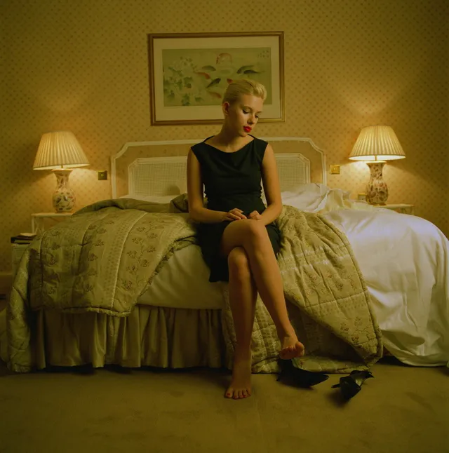 Scarlett Johansson sitting on a bed in a black dress.
