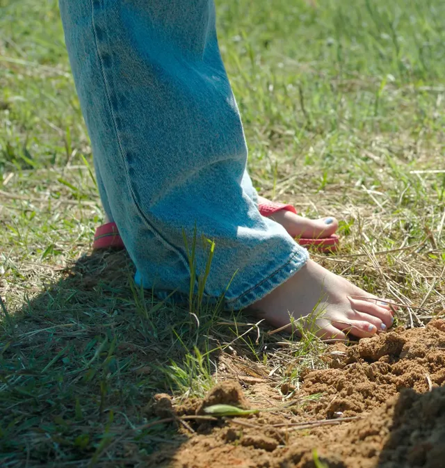 Mckenna Grace standing barefoot on grass in jeans.