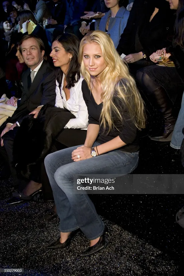 Anna Kournikova sitting in black heels and jeans in fashion-show seating.