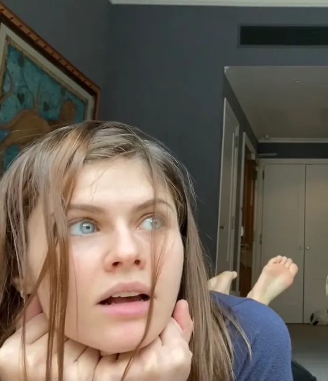 Alexandra Daddario lying indoors with a bare foot raised behind her.