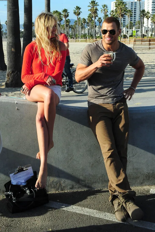 Kate Upton sitting barefoot on a wall beside a man.