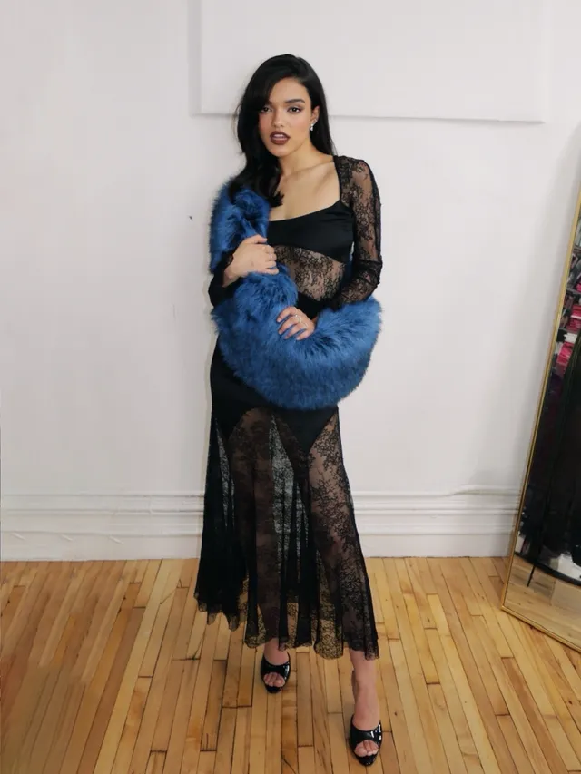 Rachel Zegler posing in a sheer black dress, blue wrap and heels.
