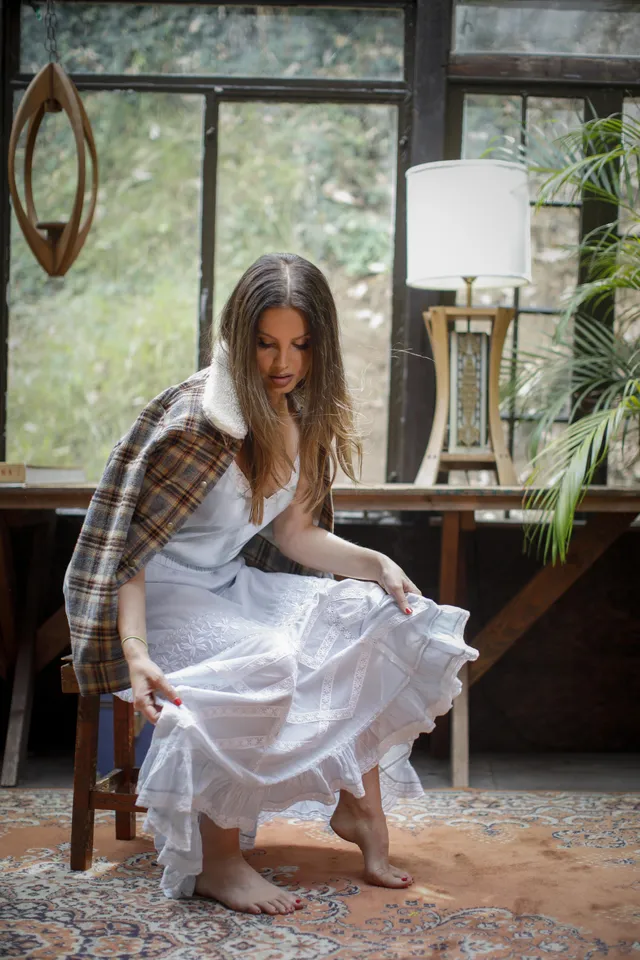 Lana Del Rey standing barefoot beside a piano in a layered skirt.