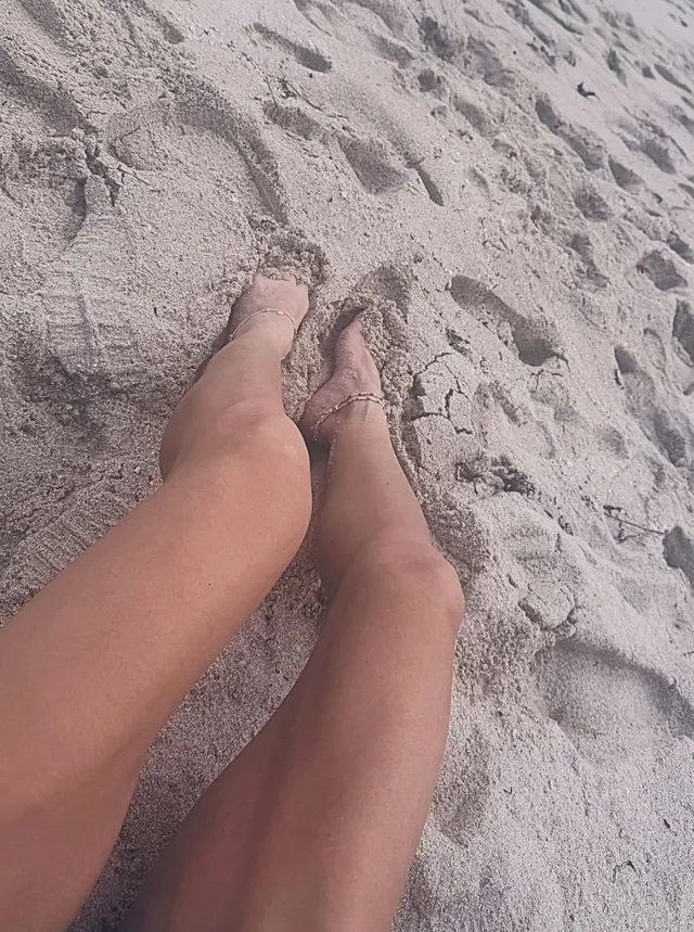 Sarah Shahi resting her bare feet on a sandy beach.