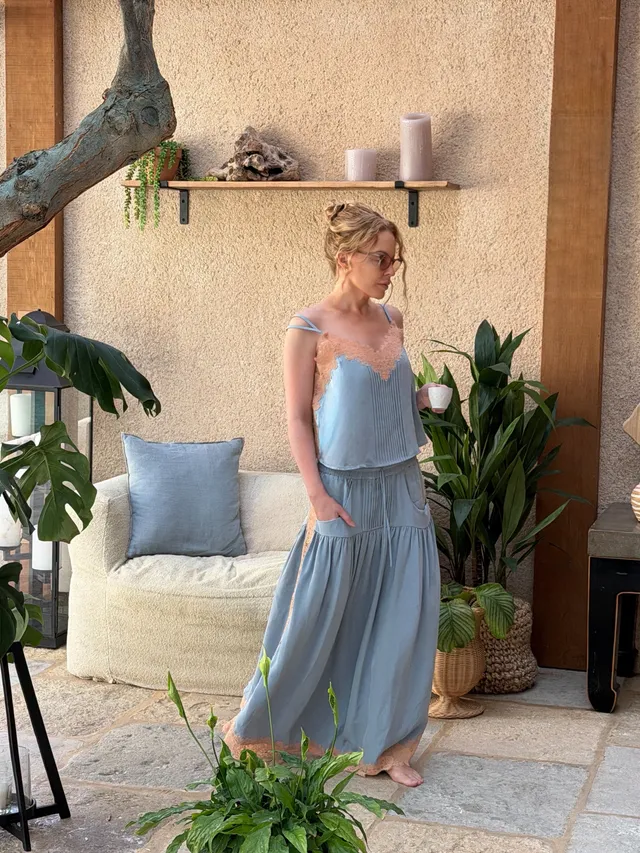 Kylie Minogue standing in a pale blue outfit beside tropical plants.