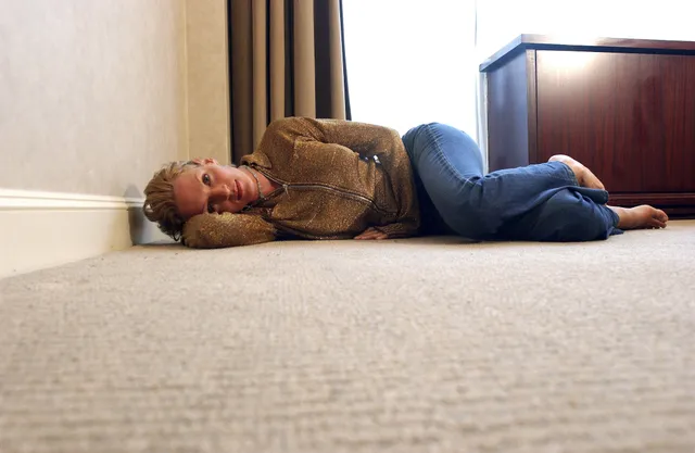 Uma Thurman reclining barefoot indoors in jeans.