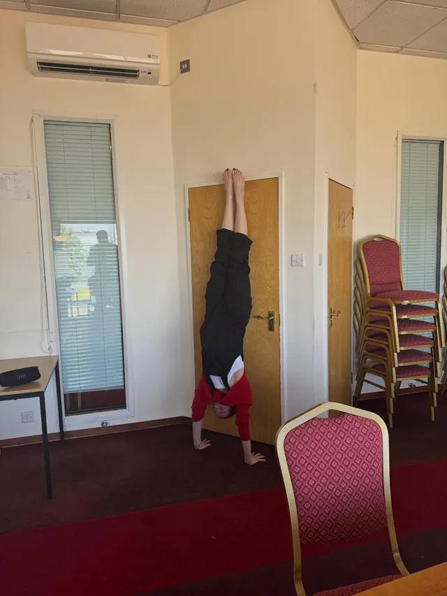 Emma Stone doing a barefoot handstand against a wall in a room with chairs.
