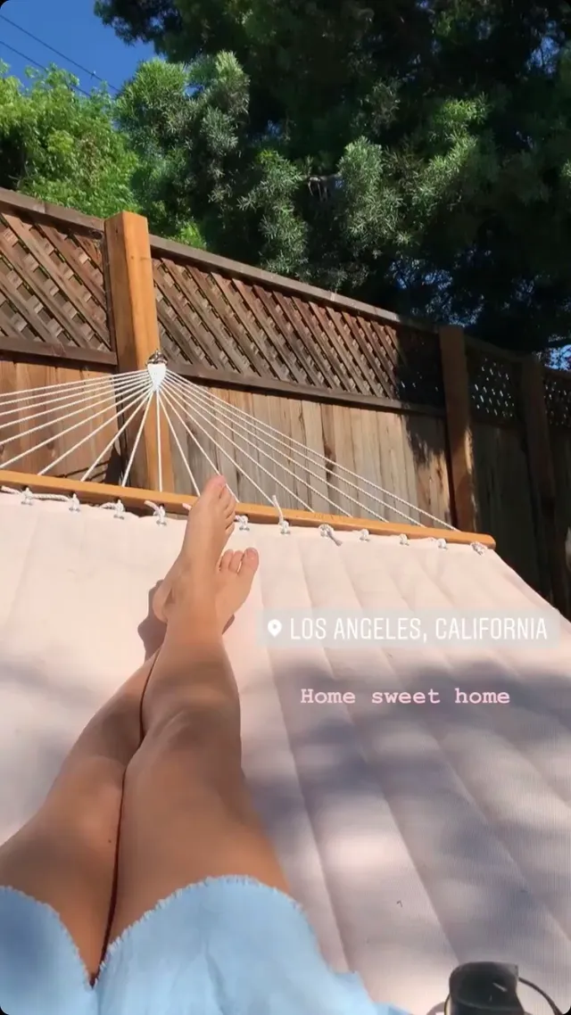 Ella Purnell relaxing in sunshine beside a wooden fence.