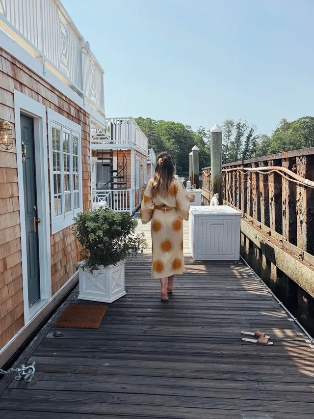 Elizabeth Gillies walking along an outdoor deck in a pale dress.
