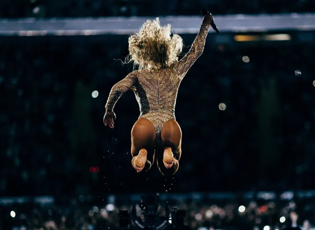 Beyoncé jumping onstage with bare soles visible from behind.