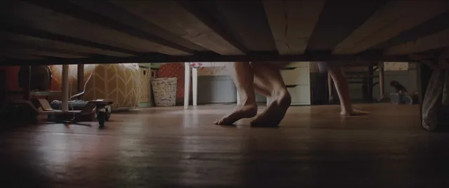 Chloë Grace Moretz with bare feet extended below a bed in a screen image.