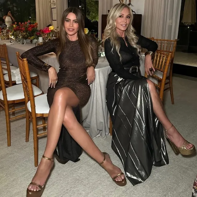 Sofía Vergara sitting beside another person in a dark dress and metallic heels.