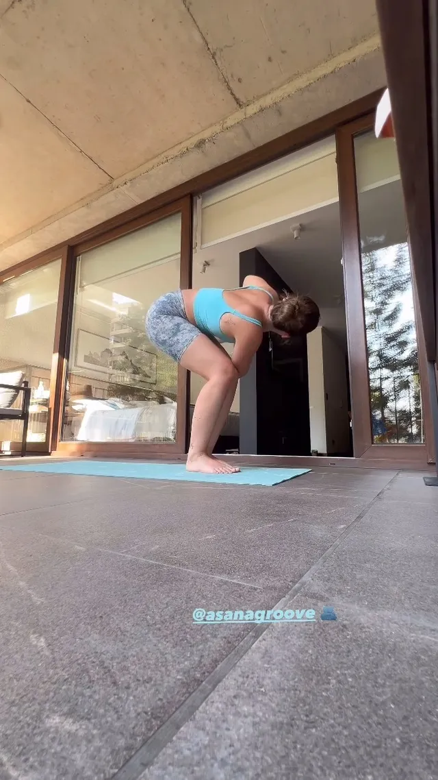Nicole Wallace crouching barefoot on a yoga mat in a blue workout outfit.