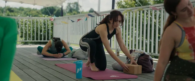 Olivia Cooke kneeling on a yoga mat outdoors in a screen scene.