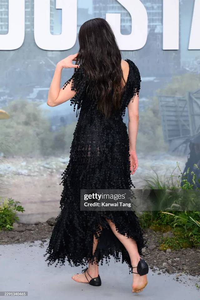 Margaret Qualley a rear premiere portrait in a black dress and heels.