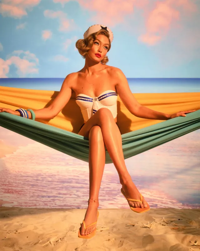 Gigi Hadid sitting in a hammock in flat sandals for a studio portrait.