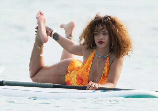 Rihanna lying on a paddleboard with one bare foot raised above the water.