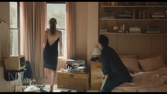 Sarah Pidgeon appearing barefoot in a black dress in a bedroom scene.
