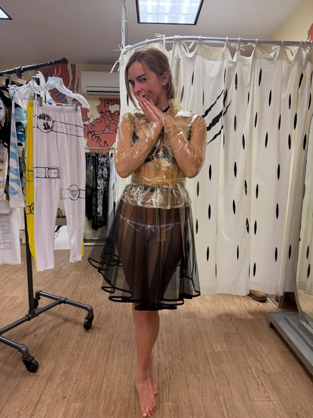 Addison Rae standing barefoot in a dressing room in a gold top and dark skirt.