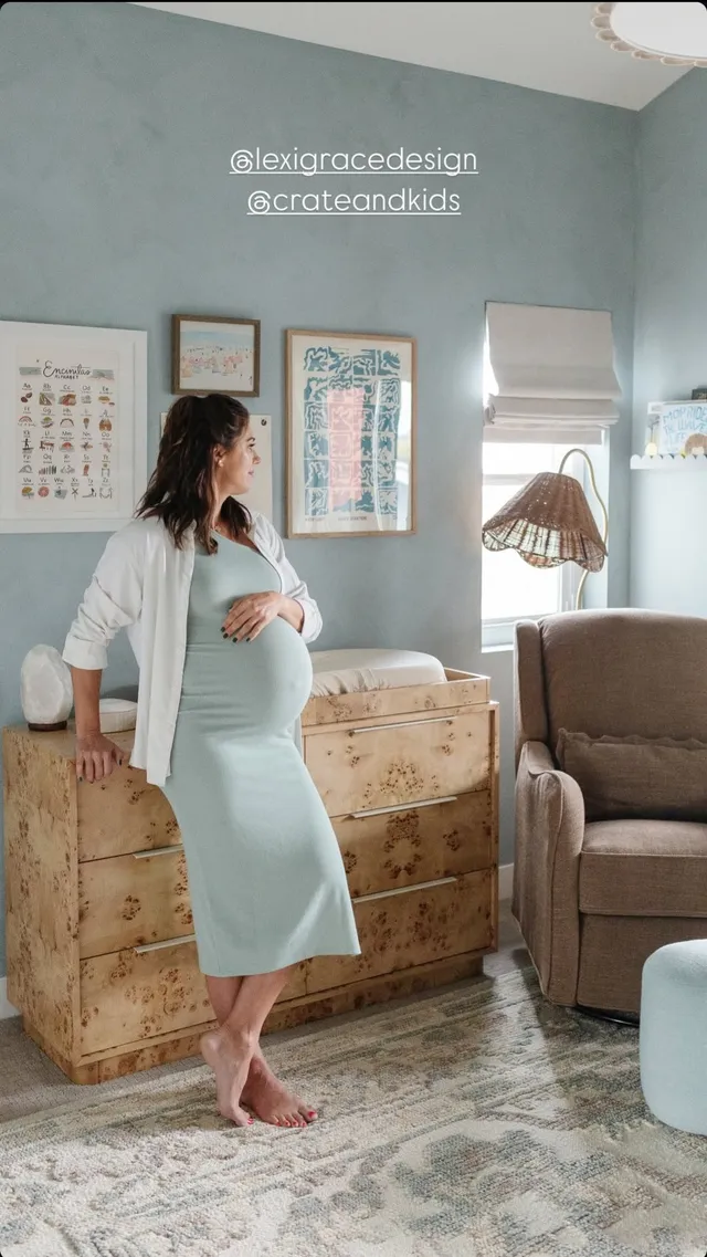 Alex Morgan standing barefoot on a rug in a pale dress during a maternity portrait.