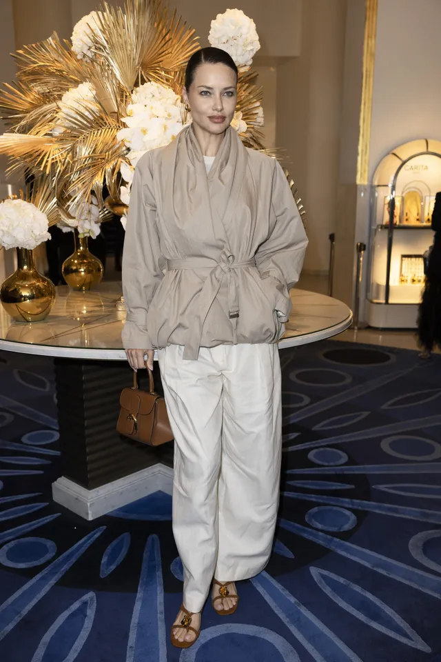 Adriana Lima posing in a pale outfit and heels at an event.