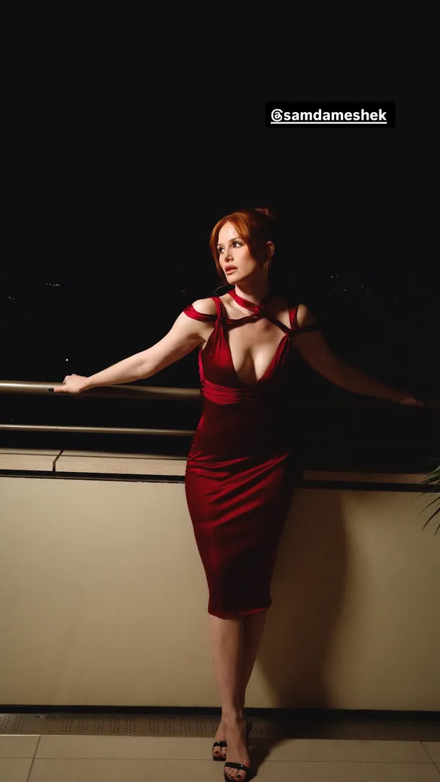 Madelaine Petsch posing in a red dress and heels against a dark backdrop.